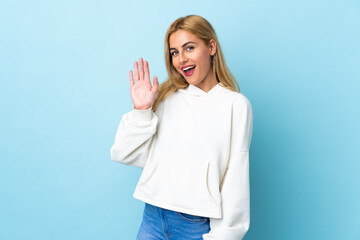 Fototapeta premium Young Uruguayan blonde woman over isolated blue background saluting with hand with happy expression