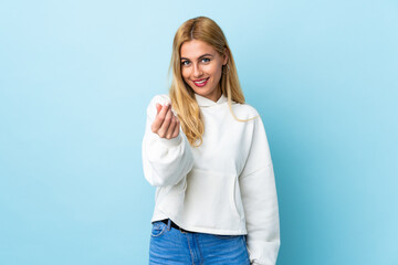 Young Uruguayan blonde woman over isolated blue background making money gesture