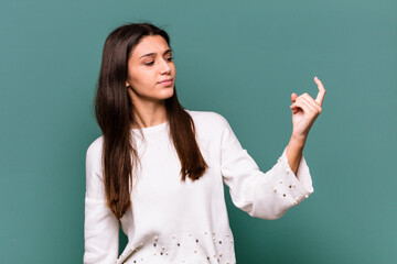 Young Indian woman isolated on blue background pointing with finger at you as if inviting come closer.