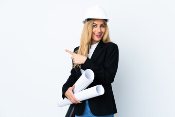 Young architect woman with helmet and holding blueprints over isolated white background pointing finger to the side
