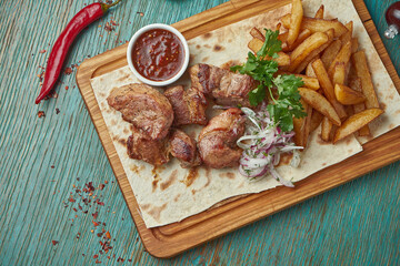 An appetizing oriental dish - grilled pork kebab with a side dish of potatoes and onions with red onions on a green background. Georgian cuisine. Shish kebab