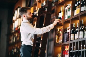 The seller of alcoholic beverages sorts bottles standing on the ladder.