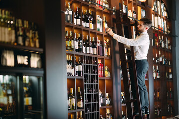 The seller of alcoholic beverages sorts bottles standing on the ladder.