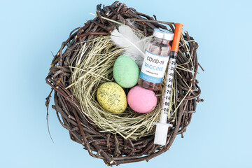 Close up view of vaccine vial, syringe and easter egg nest flatlay. Spring season concept background. Vaccination against coronavirus Covid-19 concept. 