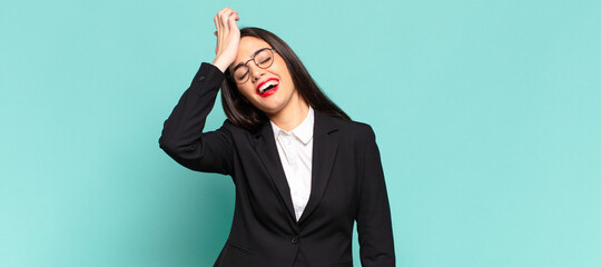 young pretty woman laughing and slapping forehead like saying d’oh! I forgot or that was a stupid...