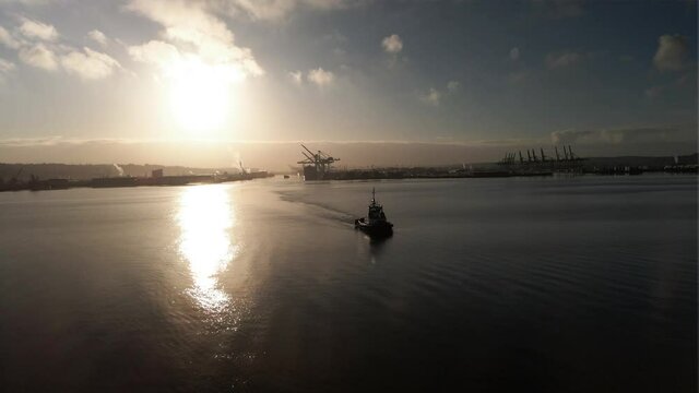 Orbiting a tugboat moving across golden sunlight reflecting off calm water, Port of Tacoma, aerial
