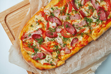 Freshly baked pizza margherita with smoked sausages, bacon, red sauce and mozzarella on a wooden tray on a gray background. Italian Cuisine