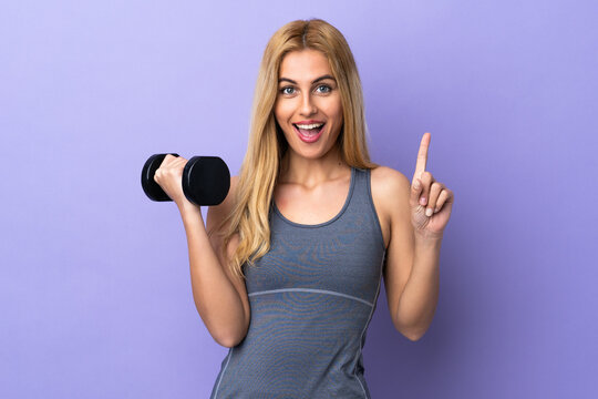 Young blonde sport woman making weightlifting over isolated purple background pointing up a great idea
