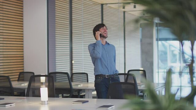 Casually dressed businessman on phone call walking through modern open plan start up office - shot in slow motion