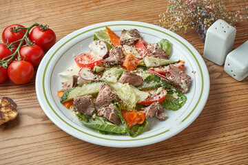 Diet and healthy salad with veal, vegetables and tomatoes, parmesan, served in a white plate on a wooden background. Restaurant food