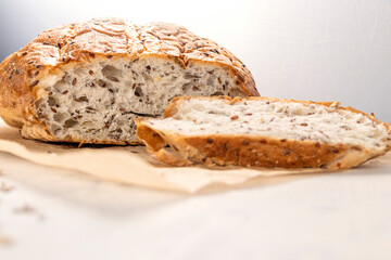 Fresh, tasty, round wheat bread with flax seeds on a white textured table with space for text. Sliced bread on serving board with flax and sunflower seeds.