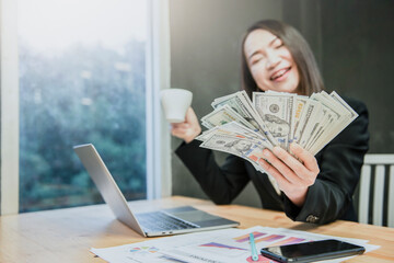 Successful beautiful business young woman holding money US dollar bills in hand on office desk,...