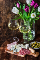Delicious snacks - ham, gorgonzola, camembert, salami, olives, white wine and a bouquet of tulips on a wooden background