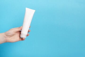 Woman's hand holding white cream tube on a blue background. Beauty concept, clean and care cosmetics.