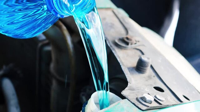 pouring blue windshield cleaning fluid into the tank of the car.