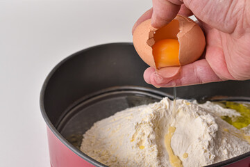 The hand of the pastry chef breaks the egg into flour. Baking dough preparation process.