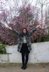 outdoors lifestyle portrait of young happy and beautiful Asian Chinese woman enjoying sakura blooming tree in pink flowers smiling playful