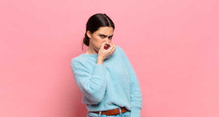 young pretty woman feeling disgusted, holding nose to avoid smelling a foul and unpleasant stench