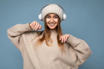 Attractive positive smiling young blonde woman wearing beige winter sweater and hat isolated over...