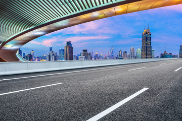 Empty asphalt road and bridge with city skyline at sunset in Shanghai.