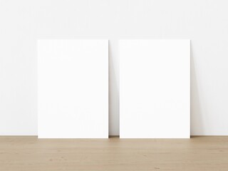 Set of two blank vertically oriented rectangular posters standing on wooden floor leaning on white wall. 3D Illustration