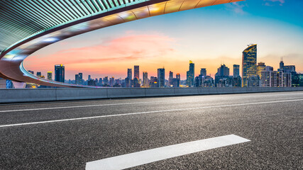 Empty asphalt road and bridge with city skyline at sunset in Shanghai.