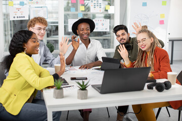 Group of five multicultural business people smiling and waving with hands during video conference on modern laptop. Young hipster colleagues having working meeting online.
