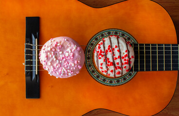 Artistic food composition of donuts on top of a acoustic guitar. Top view. Colorful cakes with sprinkles. Wood background