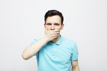 A young man dressed in a plaid blue shirt covers his mouth with his palms.