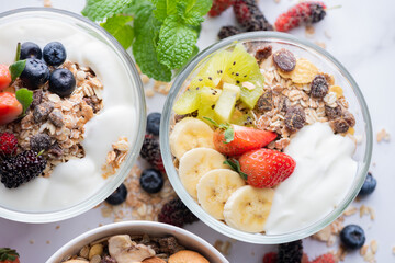 bowl of oat granola with yogurt, fresh blueberries, mulberry, strawberries, kiwi, banana, mint and nuts board for healthy breakfast, top view, copy space, flat lay. vegetarian food concept.