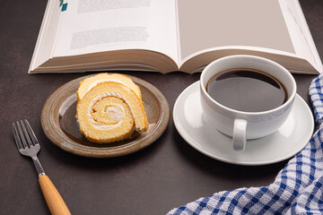 Top view of a book with roll cakes on a plate, a white coffee cup, and a cloth placed on dark gray stone background. Space for text. Concept of relaxation