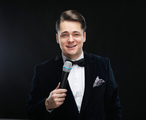 Young handsome man with microphone over black background
