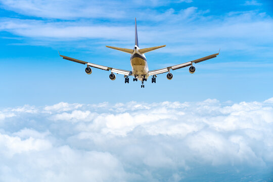 rear image commercial passenger aircraft or cargo transportation airplane flying over white fluffy cloud with blue sky and spread the wheel prepare landing to airport