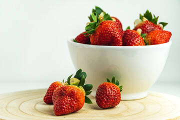 Close-up of red strawberries in a white bowl and on a wooden board.