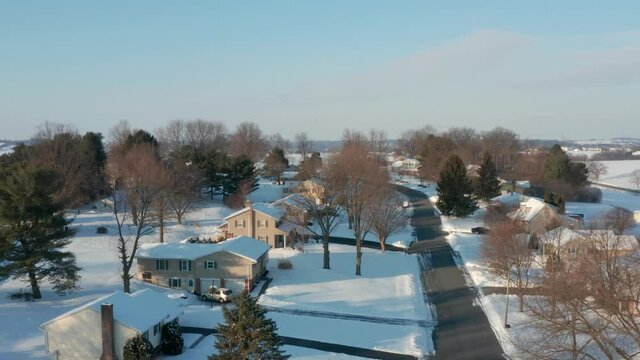Rising aerial reveals neighborhood street. Homes and houses covered in fresh winter snow. Daytime establishing shot in Northeast USA, America.