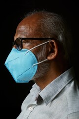 Portrait of 60 years old Indian man wearing a blue mask, isolated on a black background, in order to protect himself from COVID-19.