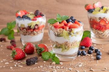 Homemade muesli, bowl of oat granola with yogurt, fresh blueberries, mulberry, strawberries, kiwi, mint and nuts board for healthy breakfast, copy space. Healthy breakfast concept. Clean eating.