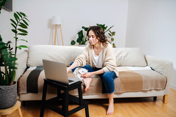 Busy young woman holding embroidering loop, watching instructions on laptop