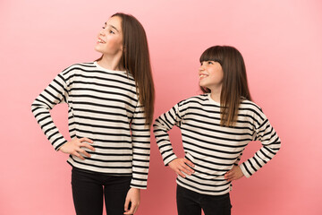 Little sisters girls isolated on pink background posing with arms at hip and laughing