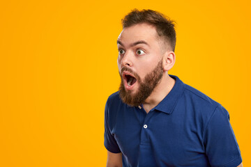 Shocked young man looking away with astonishment in yellow studio - obrazy, fototapety, plakaty