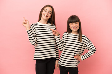 Little sisters girls isolated on pink background pointing finger to the side and presenting a product