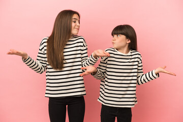 Little sisters girls isolated on pink background making unimportant gesture while lifting the shoulders