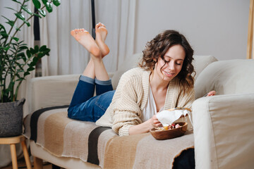 Happy young woman lying on a couch, embroidering a picture on a loop