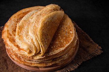 Traditional Russian food - thin pancakes. A stack of crepes on a dark brown wooden background. Rustic style.