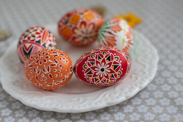 Homemade handmade painted Easter eggs on white plate dish on tablecloth with white petal flowers, Eastertime decoration