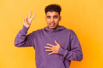 Young african american curly man isolated on purple taking an oath, putting hand on chest.