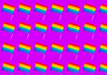 Fototapeta na wymiar Pattern of rainbow flags, representative of the gay community, on a violet background. Gay pride concept
