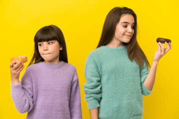 Little sisters isolated on yellow background holding a donut