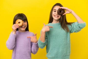 Little sisters isolated on yellow background holding a donut and happy