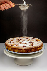 A ricotta cheese and strawberry cake on a white stand is covered with a sprinkling of icing sugar